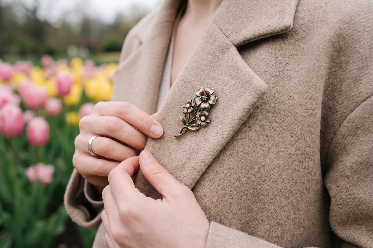 Algemene bloemvormige magneetbroche op een beige jas met tulpen op de achtergrond