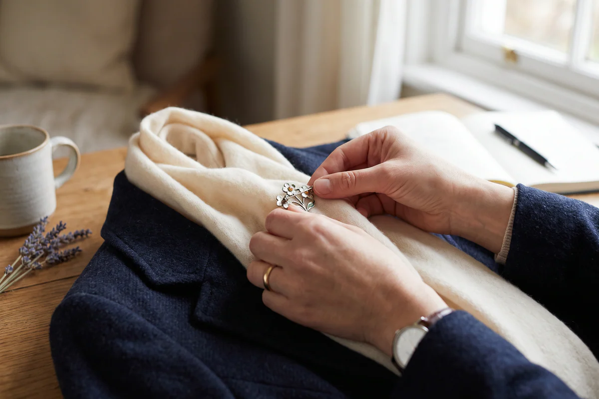 Hands placing an unbranded brooch on a cream scarf over a navy coat