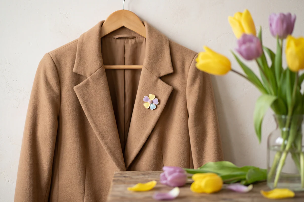 A flower-shaped magnetic accessory on a camel coat beside spring tulips