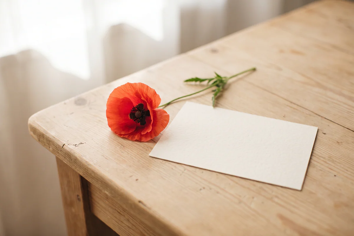 Papoila vermelha e cartão em branco numa mesa de madeira clara