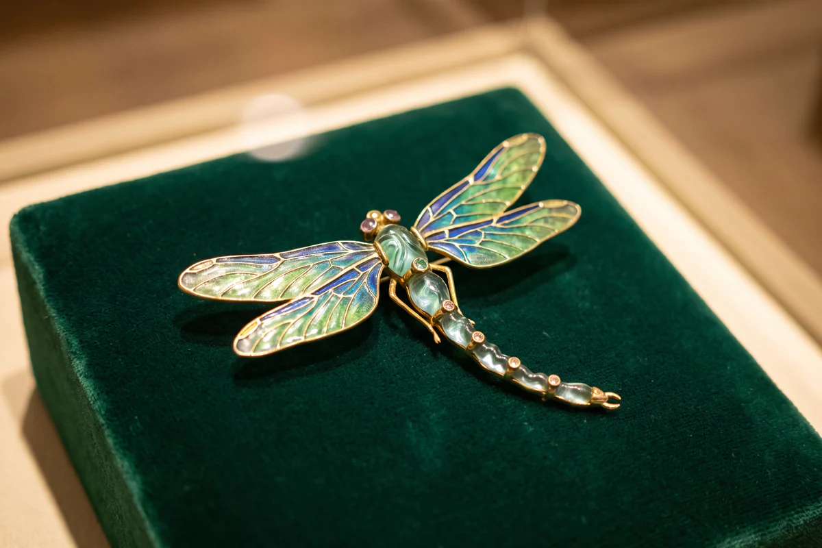 Libellen-Schmuckstück im Jugendstil mit grün und blau emaillierten Flügeln auf dunklem Samt