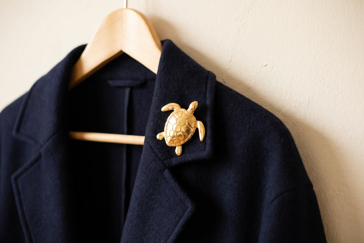 Broche tortue de couleur dorée sur le revers d’une veste bleu marine suspendue à un cintre en bois