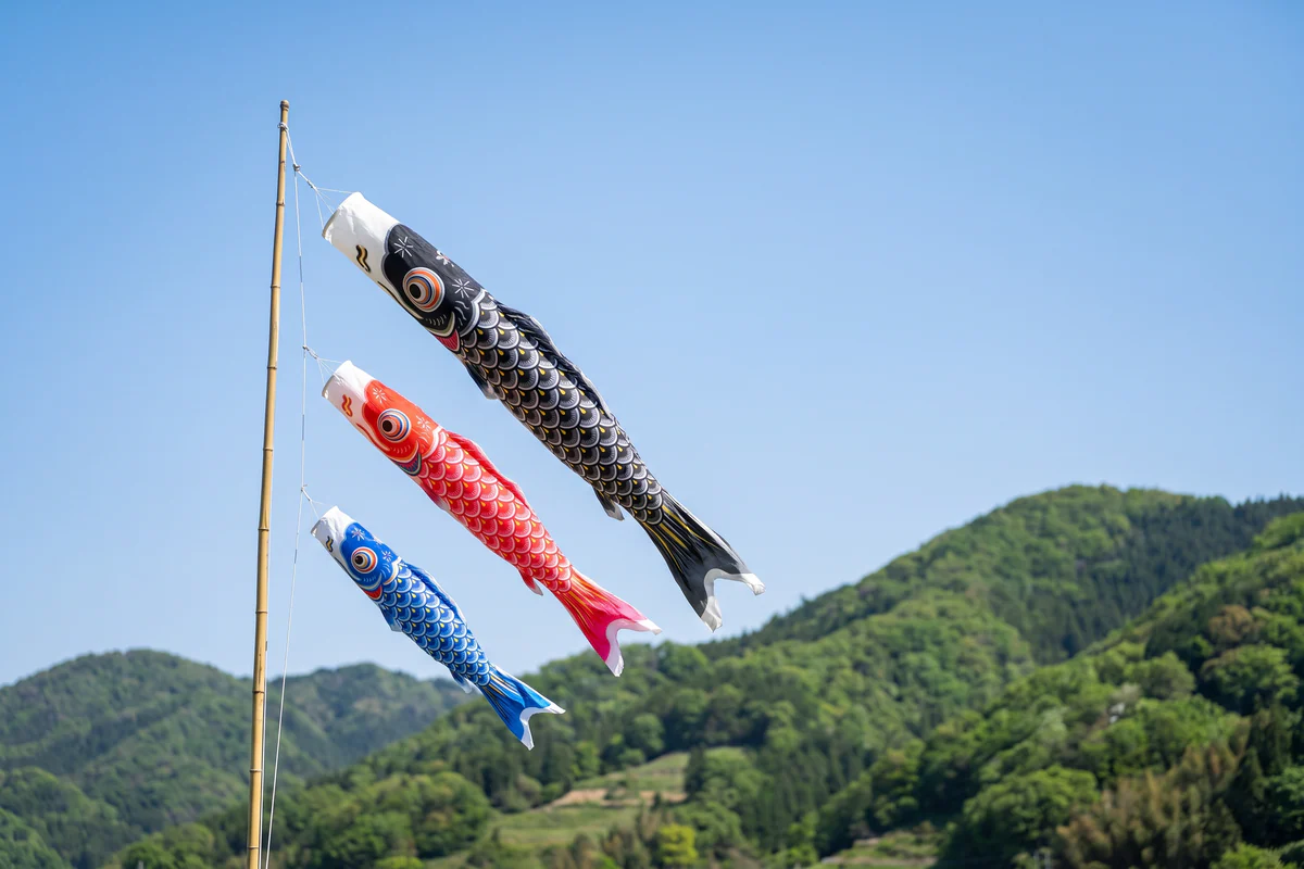 Schwarze, rote und blaue Koinobori-Karpfen im Wind an einer Bambusstange